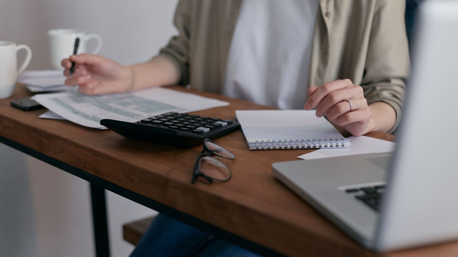 Person at a desk with a laptop, calculator, notebook, and papers.