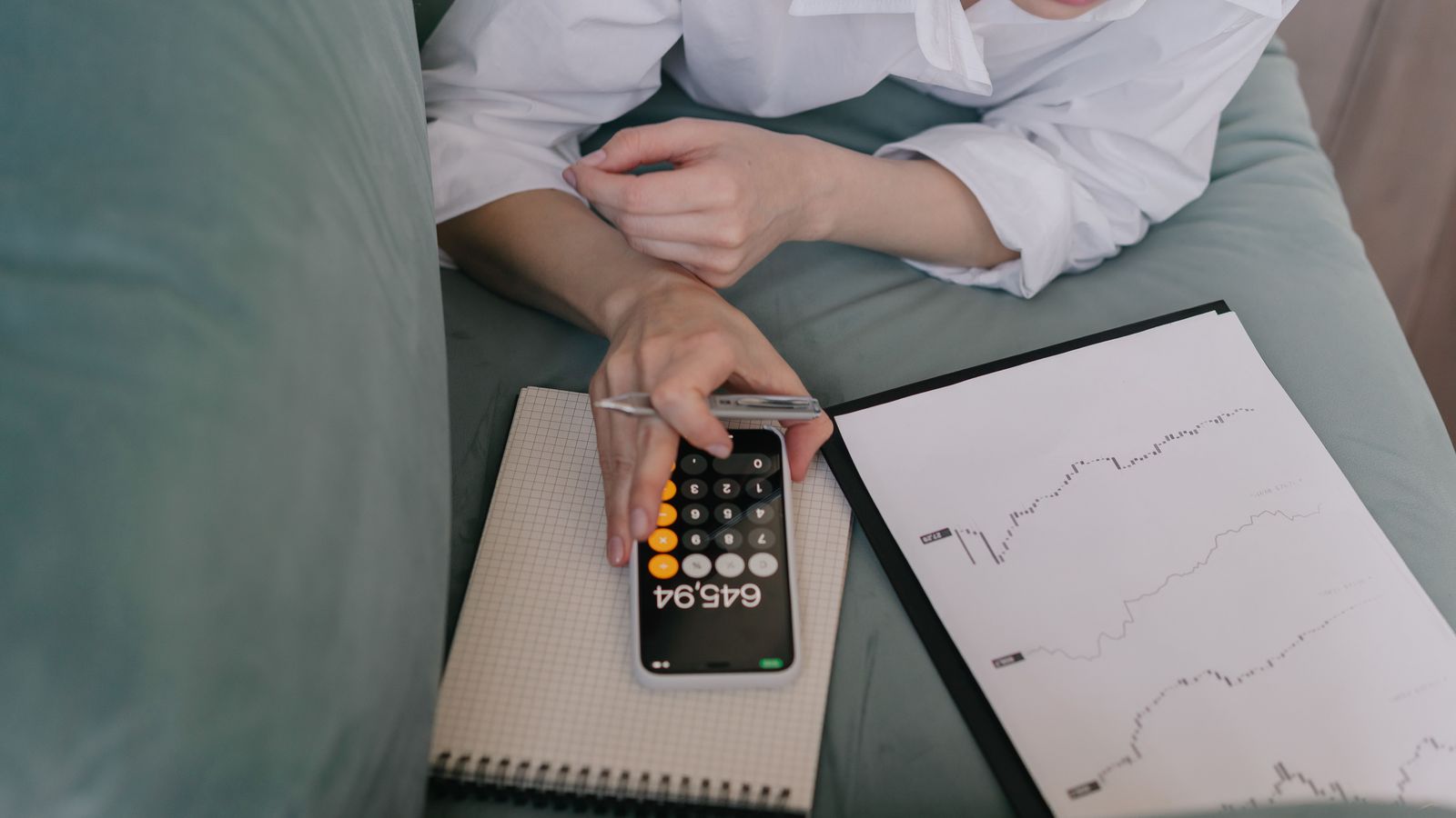 Person using a phone calculator beside investment charts on a couch.